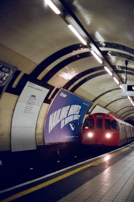 A large, historic railway station building with ornate architectural details, including arched windows and decorative stonework, situated in Belsize Park. In front of the station, there is a spacious 